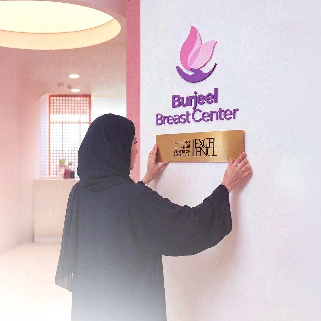 A visitor placing the Department of Health, Abu Dhabi Center of Excellence plaque beneath the Burjeel Breast Center wall logo.